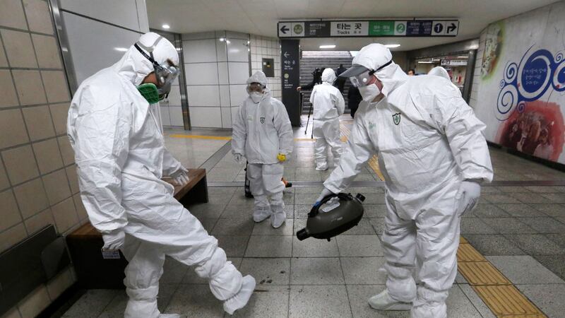 Workers wearing protective gear help clean each other's suits after disinfecting as a...